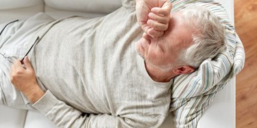 Man with migraine laid on sofa holding his head