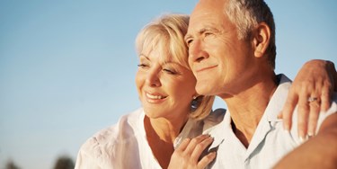 Older couple smiling and looking into the distance with a warm evening sun on their faces