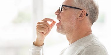 Man taking pill wearing glasses and holding glass of water