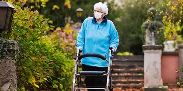 Woman wearing mask and using a walking frame taking a socially distanced walk in the fresh air