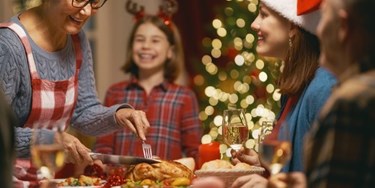 Family smiling and enjoying a Christmas dinner as someone carves the turkey