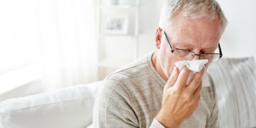 Man in living room holding tissue over his nose