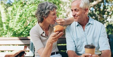 Older couple enjoying coffee and muffins on a bench outside